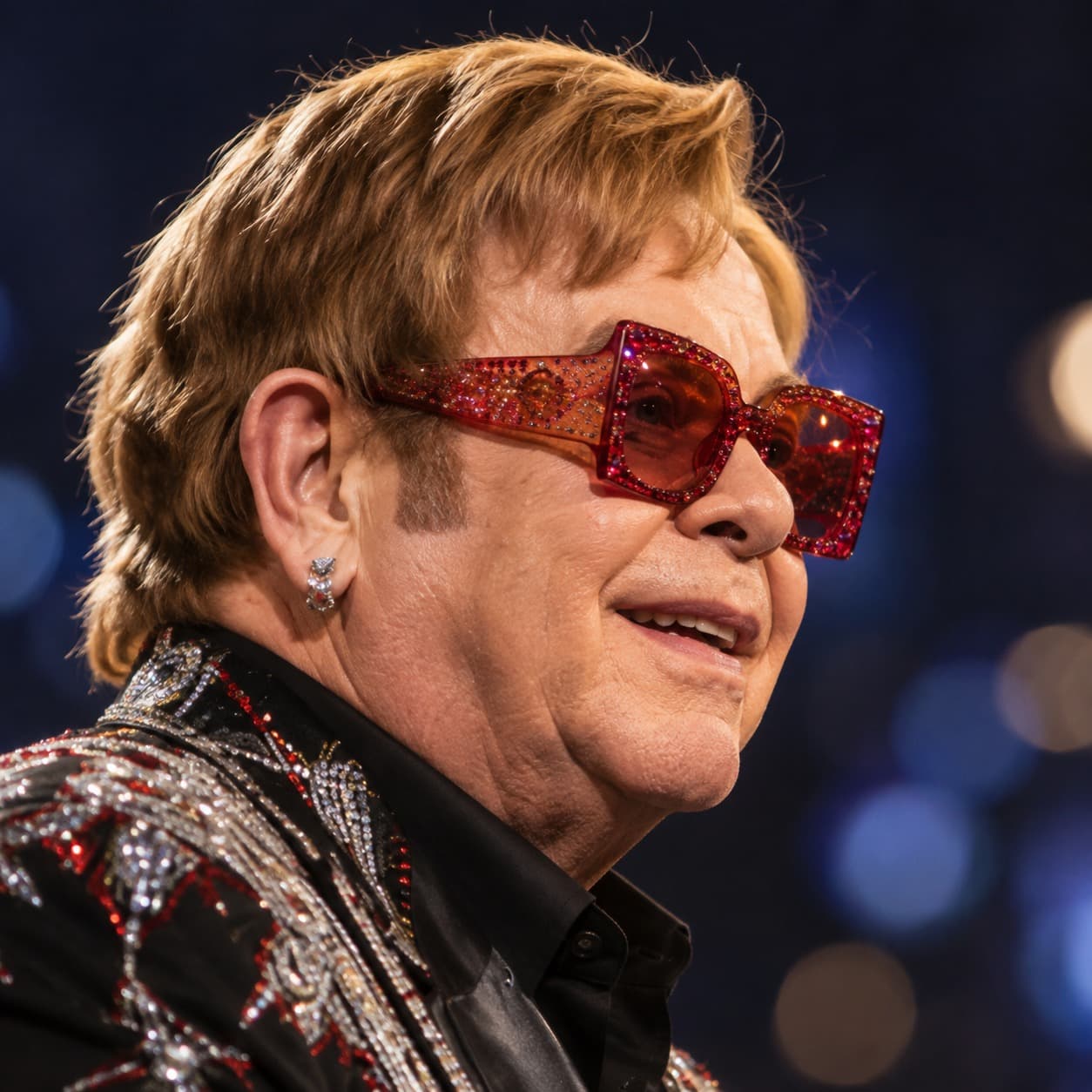 Retrato de Elton John de perfil, com óculos vermelhos cravejados e paletê bordado